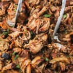 square image of slow cooker carnitas with tongs picking some up