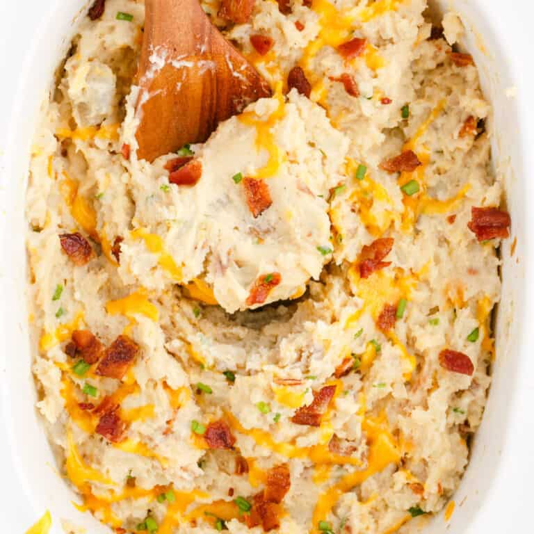 square image of a wooden spoon in stirred slow cooker loaded mashed potatoes in the crock pot