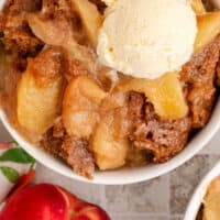 looking down at slow cooker peach cobbler topped with ice cream with recipe name at the bottom