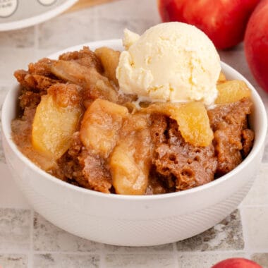 square image of slow cooker peach cobbler in a bowl topped with vanilla ice cream