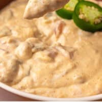 tortilla chip being lifted from a bowl of slow cooker queso dip with recipe name at the bottom