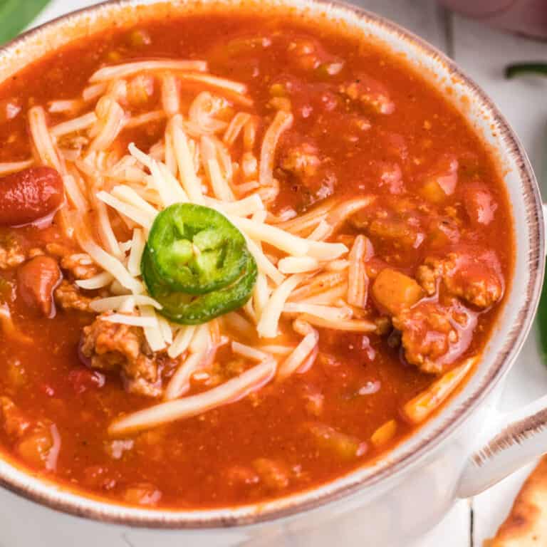 square image of slow cooker wendy's chili in bowl topped with shredded white cheddar cheese and jalapeno slices