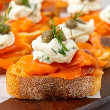square side view image of smoked salmon crostini on a wooden serving board