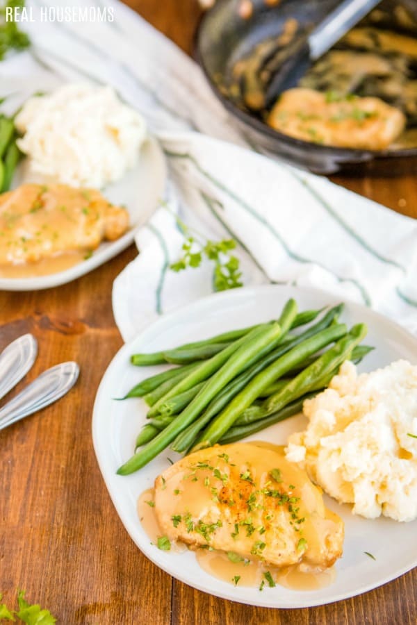 smothered fried pork chops served on a plate with mashed potatoes and green beans