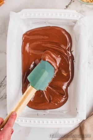 melted chocolate and peanut butter mixture being spread in a parchment paper-lined baking dish