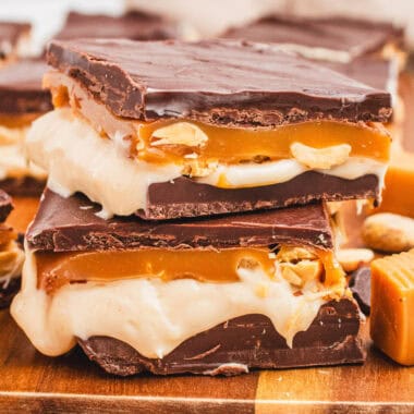 square image of two snickers cheesecake bars stacked up on a cutting board