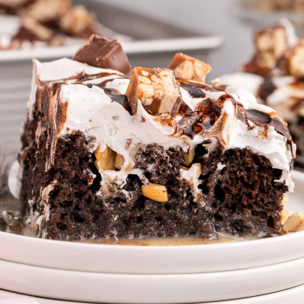 square image of a slice of snickers poke cake on a plate