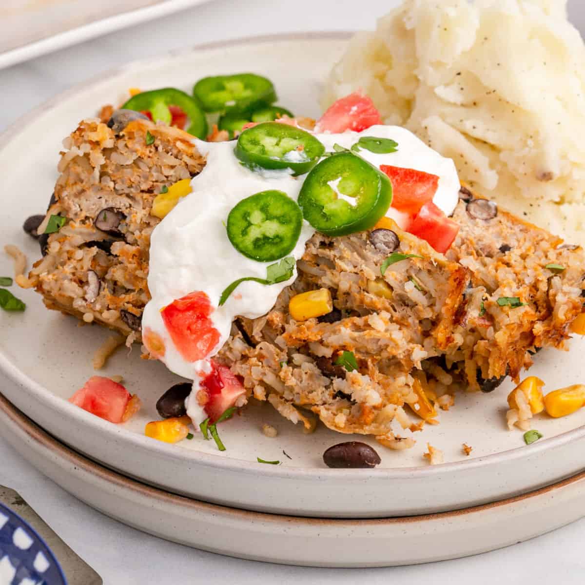 square image of slices of southwest turkey meatloaf on a plate with mashed potatoes