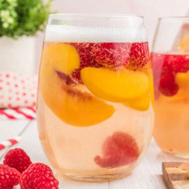 square image of sparkling white peach sangria topped with champagne in a wine glass