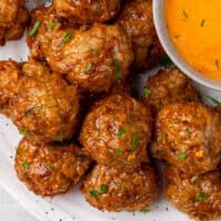 spicy chicken meatballs piled on a plate next to a bowl of buffalo ranch sauce with recipe name at the bottom