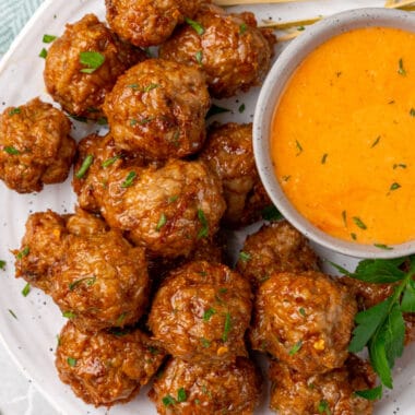 square image of spicy chicken meatballs on a plate with a bowl of buffalo ranch sauce