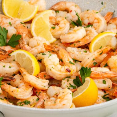 square image of spicy garlic shrimp in a skillet with lemon wedges