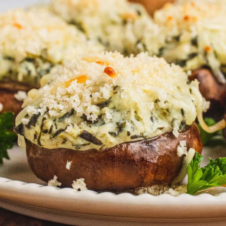 square close up image of spinach dip stuffed mushrooms on a plate