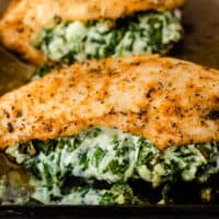 three spinach stuffed chicken breasts on a baking sheet with recipe name at bottom