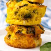 three spinach and cheese breakfast egg bites stacked up with a bite taken out of the top one with recipe name at the bottom