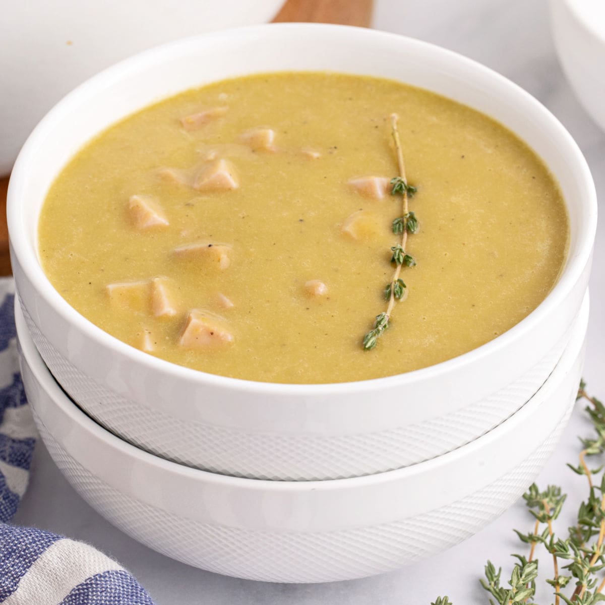 square image of a bowl of split pea soup with a thyme sprig for garnish