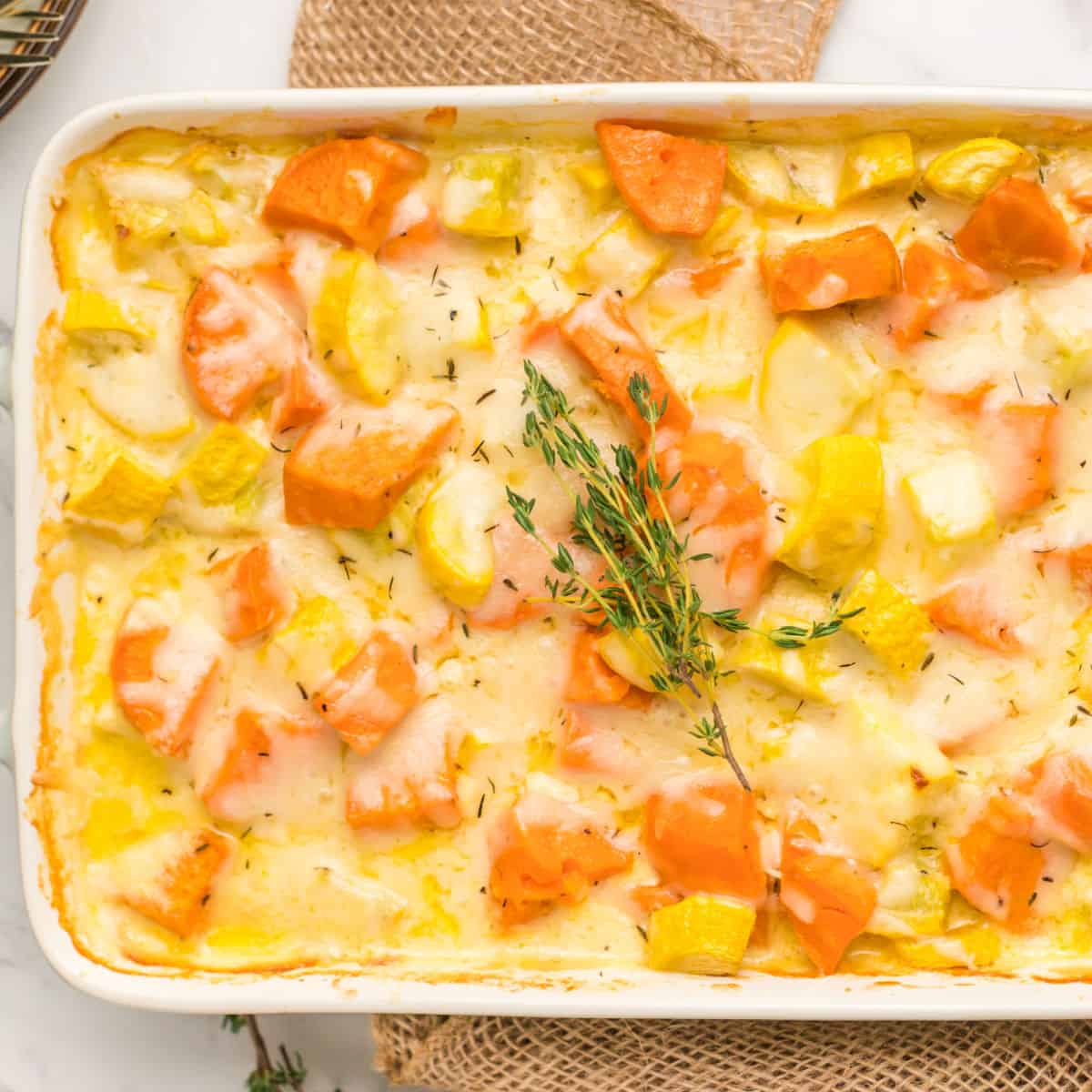 square image of squash & sweet potato gratin in a baking dish with sprigs of thyme on top