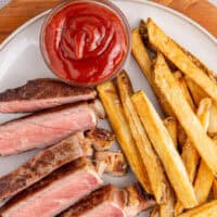 image of steak frites on a plate with a small bowl of ketchup for dipping with the title of the post on top of the image in blue and black lettering