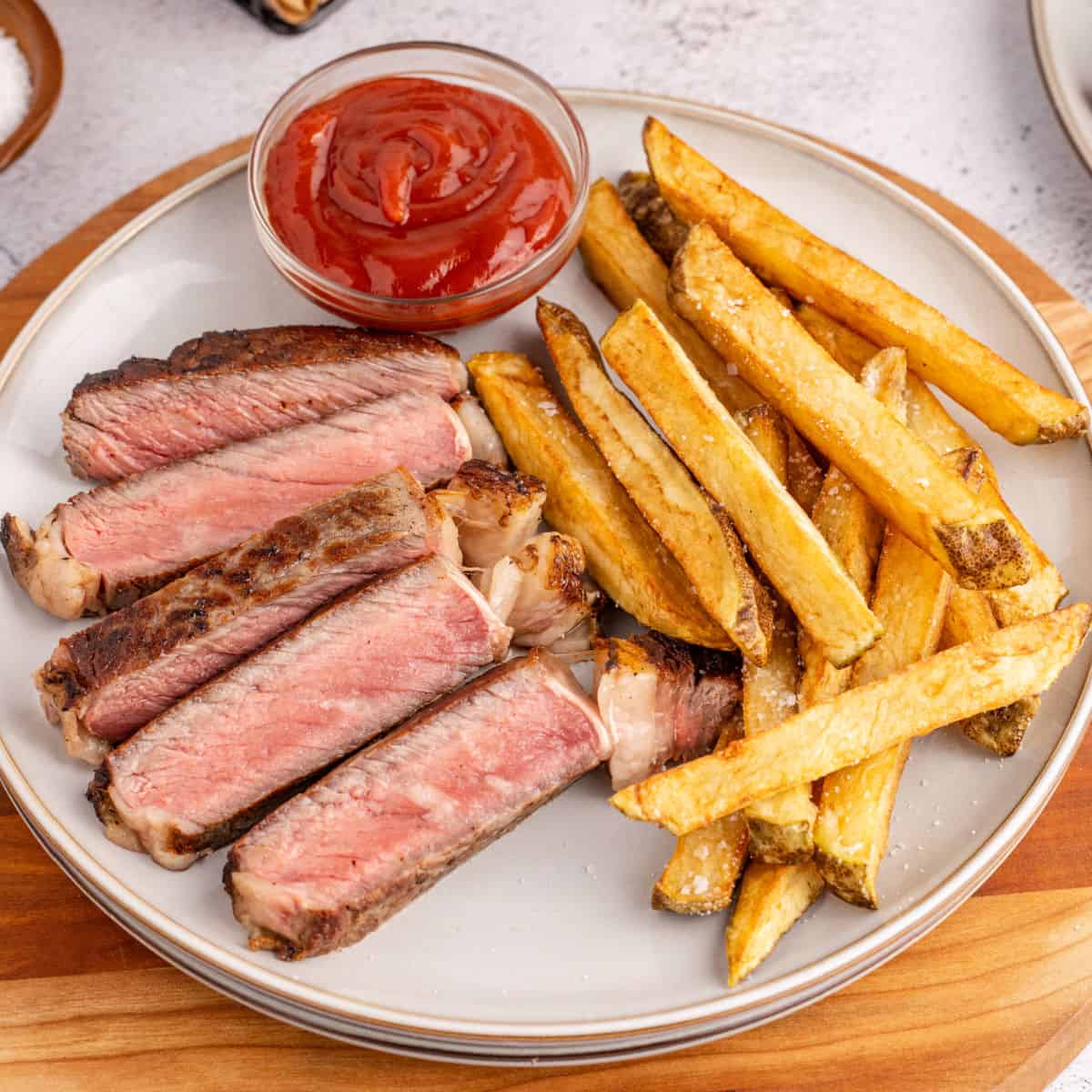 square image of steak frites on a plate with a small bowl of ketchup for dipping