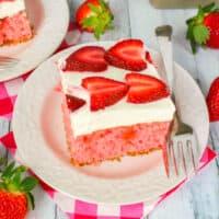 slice of strawberries & cream poke cake on a plate next to the cake and basket of strawberries with recipe name at the bottom