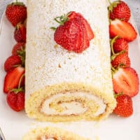 top view of strawberries and cream swiss roll with a slice cut front to show the swirl inside with the title of the post on top of the image in red and black lettering