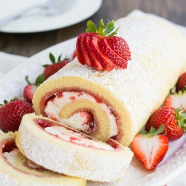 square image of strawberries and cream swiss roll on a plate with slices cut from the front