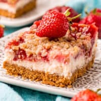 square image of a strawberry cheesecake bar on a plate with a strawberry on top