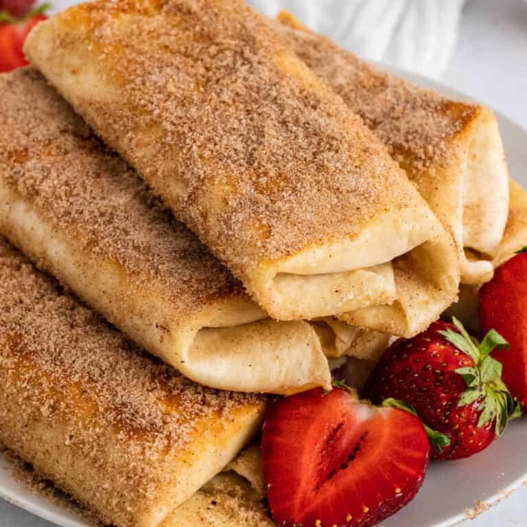 square image of strawberry cheesecake chimichangas piled on a plate with halved strawberries
