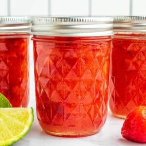 square image of jars of strawberry freezer jam next to limes and strawberries