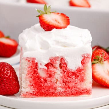 square image of a slice of strawberry poke cake on a plate with fresh strawberries