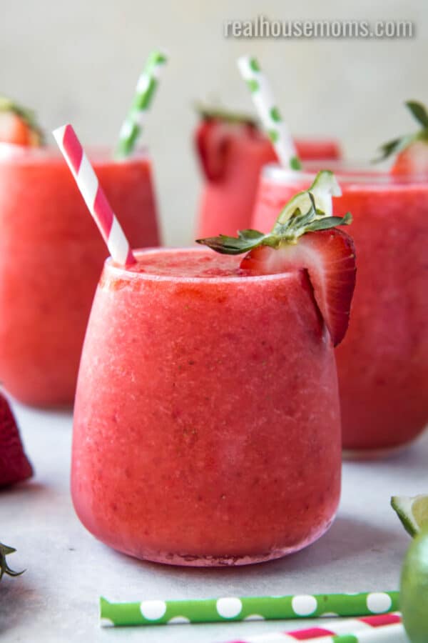 three strawberry & lime moscato wine slushies in glasses with a straw and strawberry on the rim