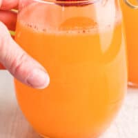 hand reaching for a glass of strawberry mango moscato punch with recipe name at bottom