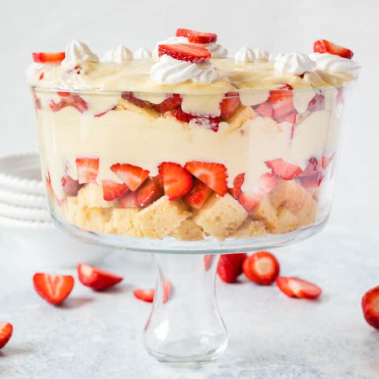 square image of a strawberry shortcake trifle in a trifle bowl surrounded by strawberries