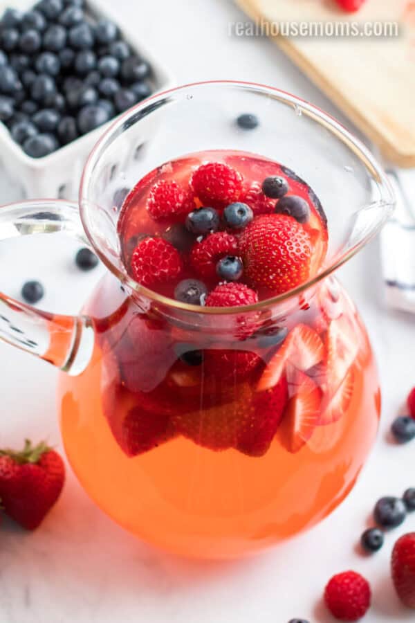 This stunning Summer Berry Sangria takes easy sangria recipes to another level! The sweet white wine and summer fruits combine for the BEST summer drink! summer berry sangria in a glass pitcher with fresh berries