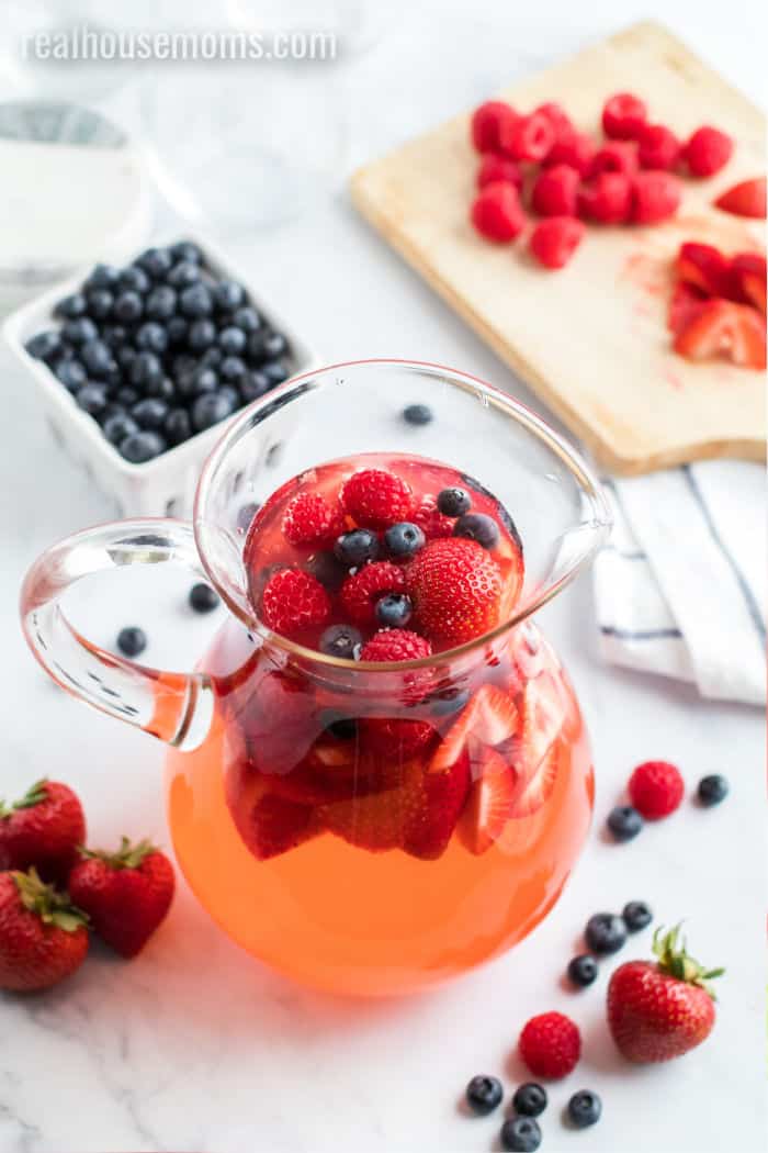 summer berry sangria in a pitcher with blueberries, strawberries, and raspberries