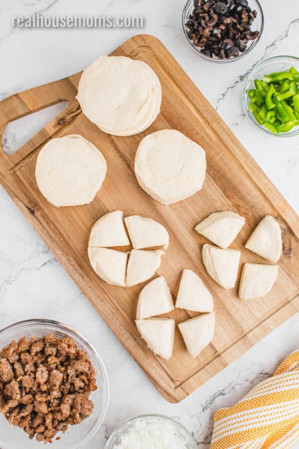 refrigerated biscuits separated and cut into quarters on a cutting board