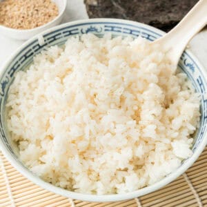 square image of sushi rice in a serving bowl with a rice paddle