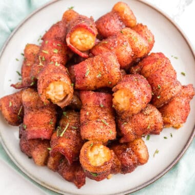 square image of sweet bacon wrapped tater tots piled on a plate with chopped parsley on top