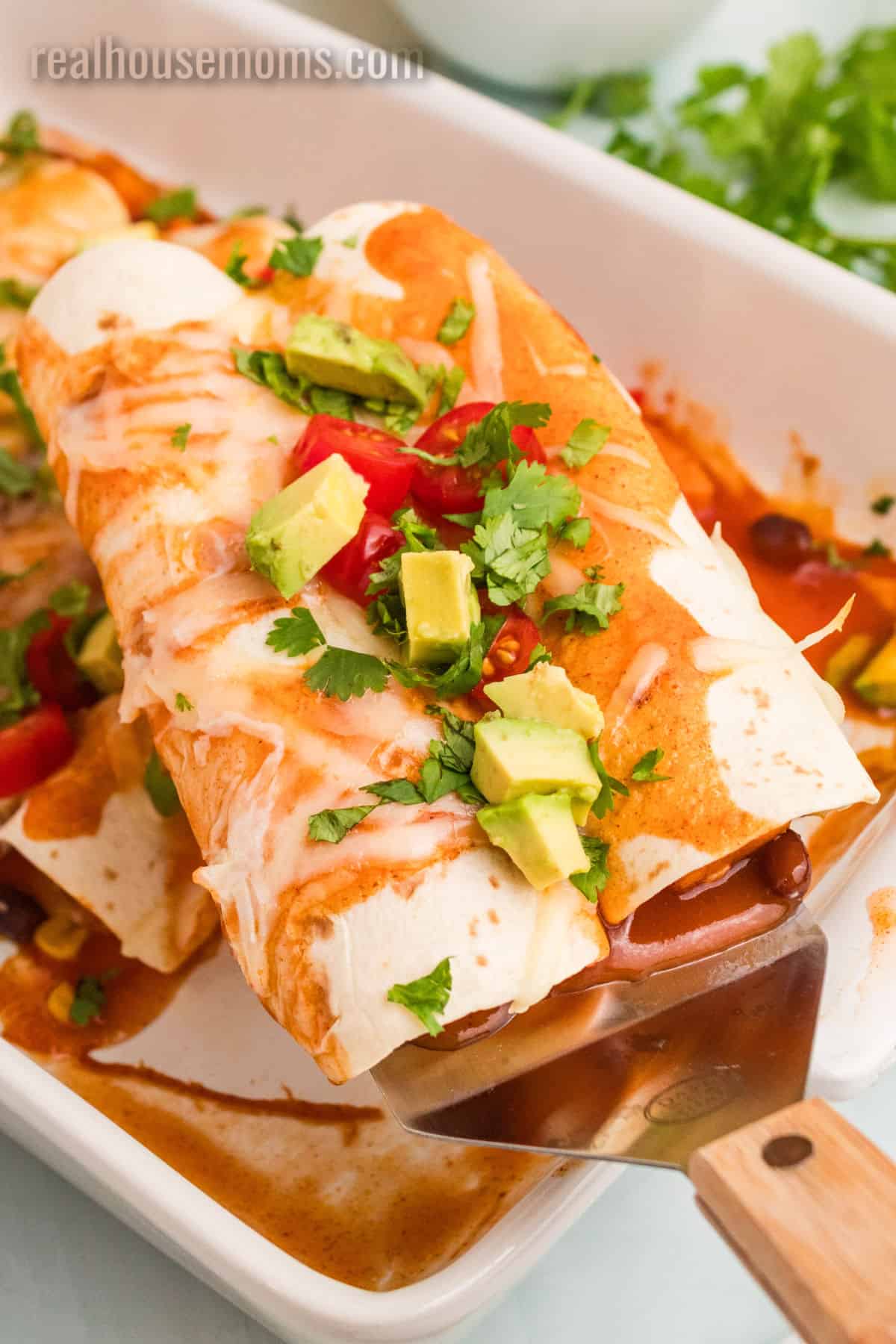 two sweet potato black bean enchiladas on a spatula over the baking dish