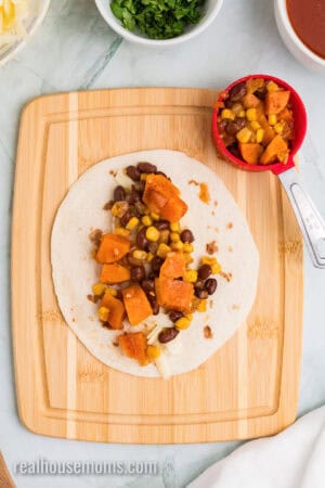 shredded cheese and sweet potato black bean enchilada filling arranged down the center of a tortilla on a cutting board