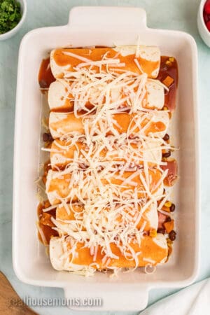 sweet potato black bean enchiladas in a baking dish covered with red enchilada sauce and shredded cheese