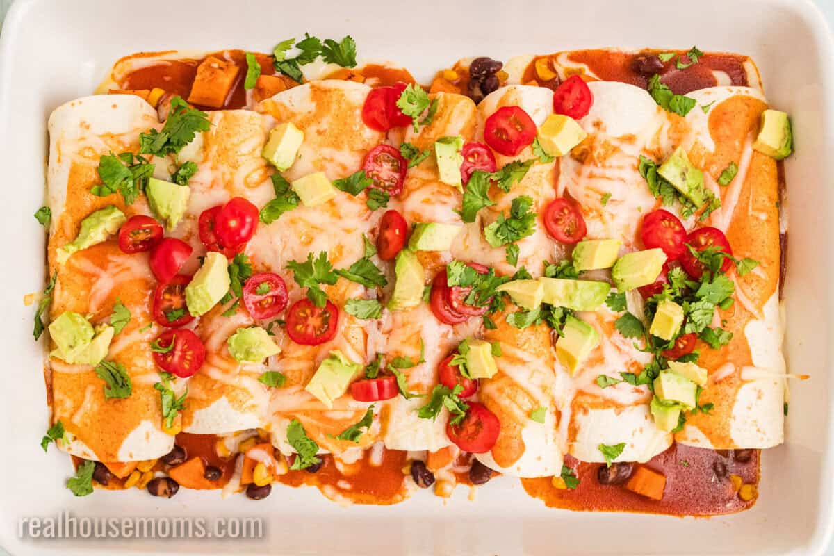 looking down at a pan of sweet potato black bean enchiladas topped with avocado, tomato, and cilantro