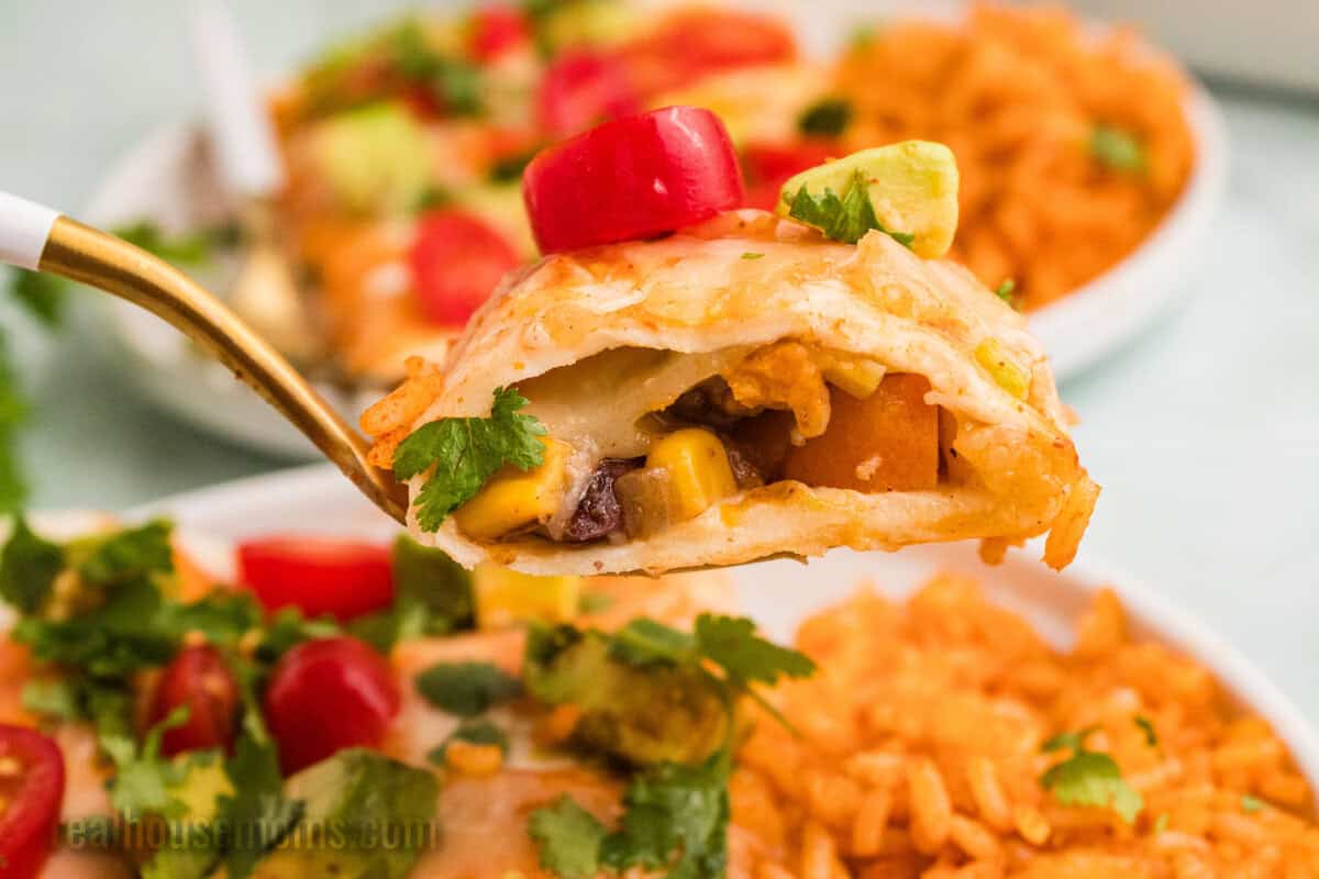 bite of sweet potato black bean enchilada on a fork over the plate