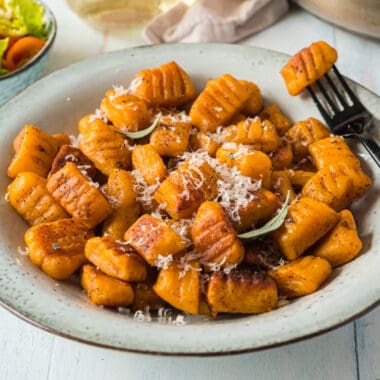 square image of sweet potato gnocchi in a bowl topped with parmesan and fresh sage