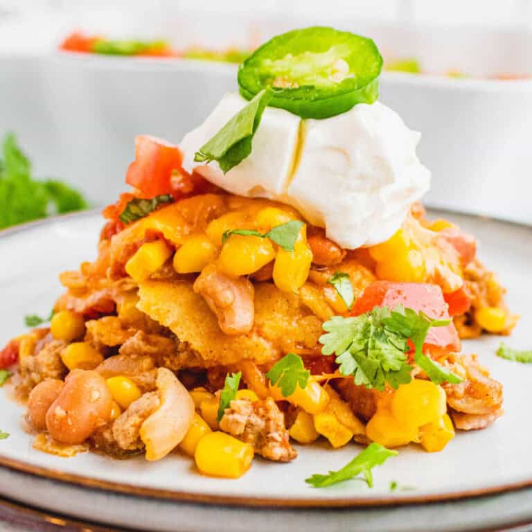 square image of a portion of taco casserole bake topped with sour ream, a jalapeno slice, and cilantro
