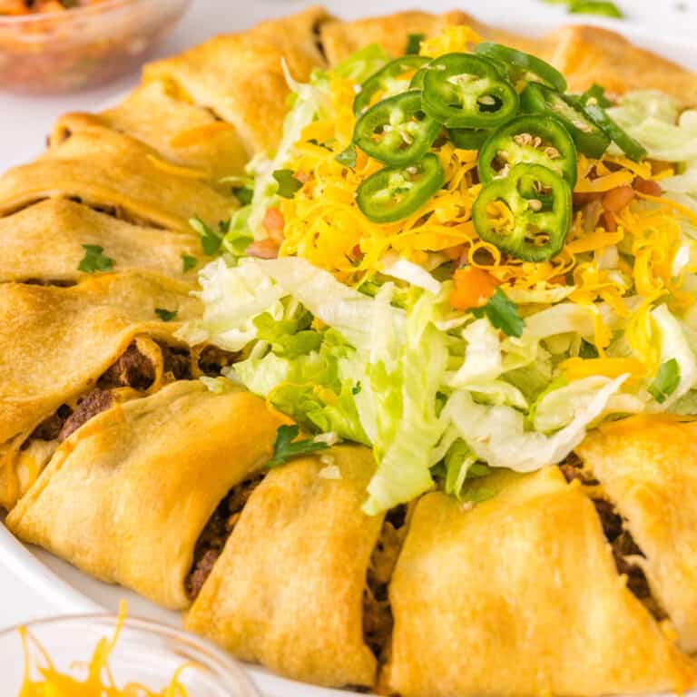 square image of taco crescent roll ring with lettuce, tomato, cheese, and jalapeno in the middle