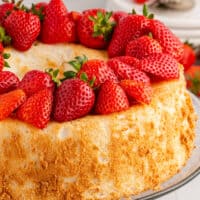 picture of angel food cake topped with strawberries on a cake stand with the title of the post on the top with blue and black lettering