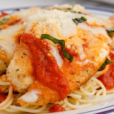 square image of tilapia parmesan on a plate of spaghetti