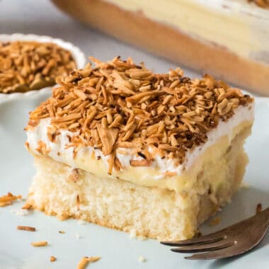 square image of a slice of toasted coconut poke cake on a plate with a fork