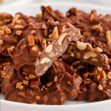square image of toffee peanut clusters piled on a plate with one broken in half to show the inside